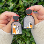 Polymer clay earrings design of two calico cats seating in a window watching snow fall 
