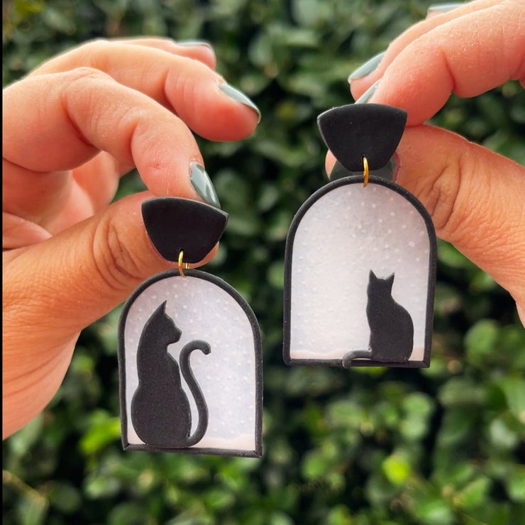 Polymer clay earrings design of two black cats seating in a window watching snow fall 